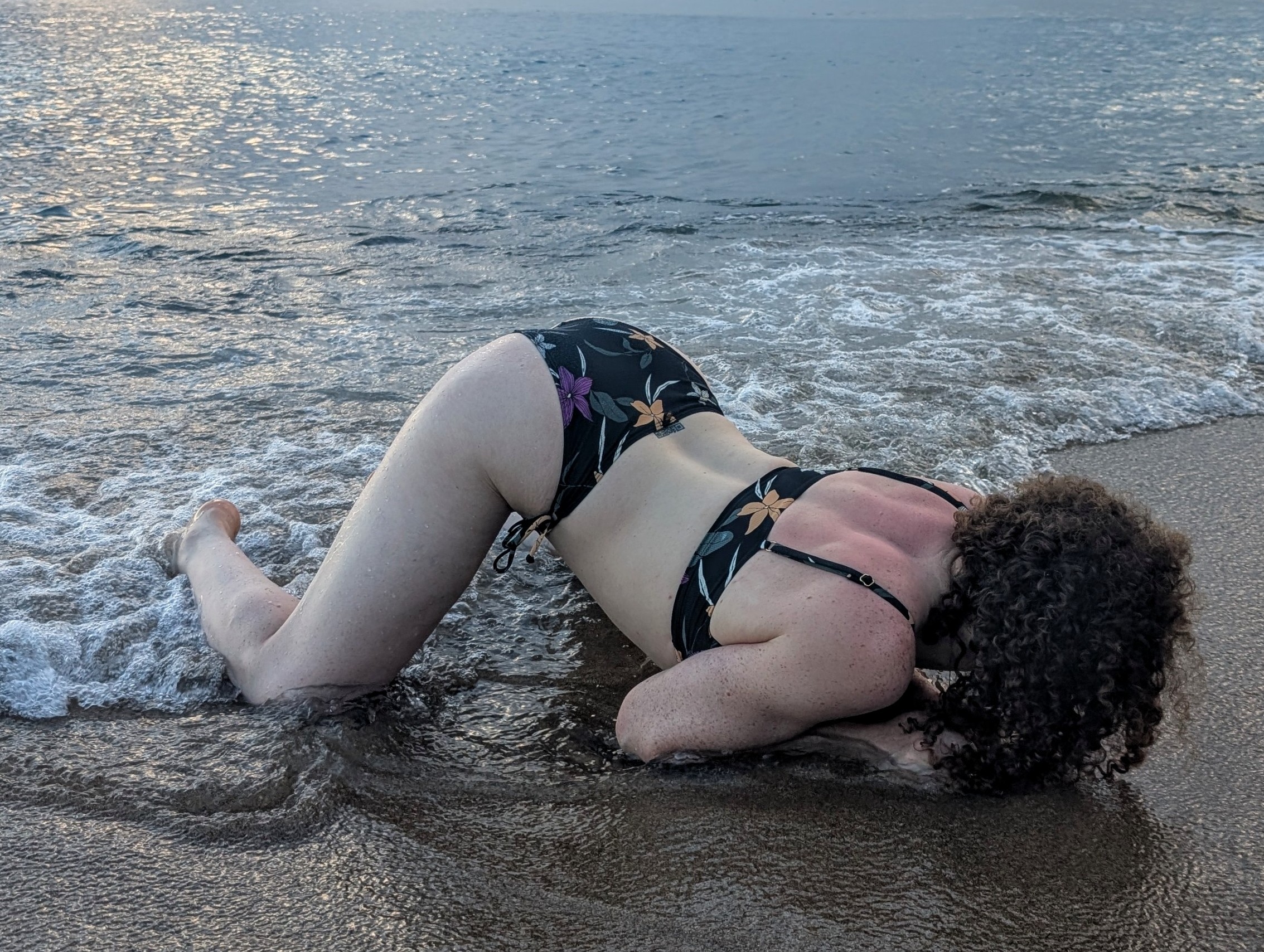 Violet relaxes in the sands of a beach on all fours as she enjoys the waves.
