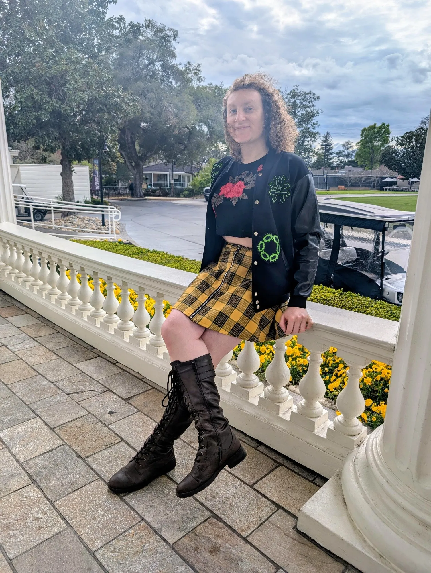 Violet sits on the bannister at a resort while wearing a leather jacket embroidered with numerous cryptocurrency industry logos.
